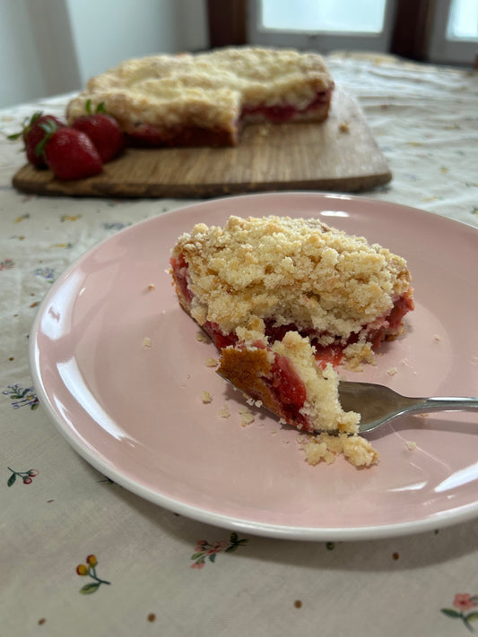 Piece of Strawberry Rhubarb Cake on a pink plate with the whole cake and some strawberries in the background