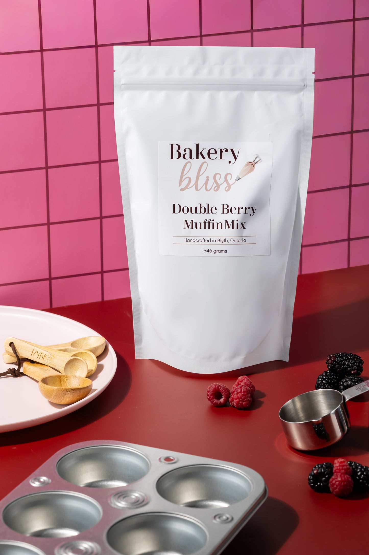 Bakery bliss Double Berry Muffin Mix packaging on a red surface with baking tools and berries.