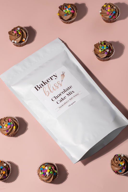 Bag of Bakery Bliss chocolate cake mix with decorated cupcakes on a pink background