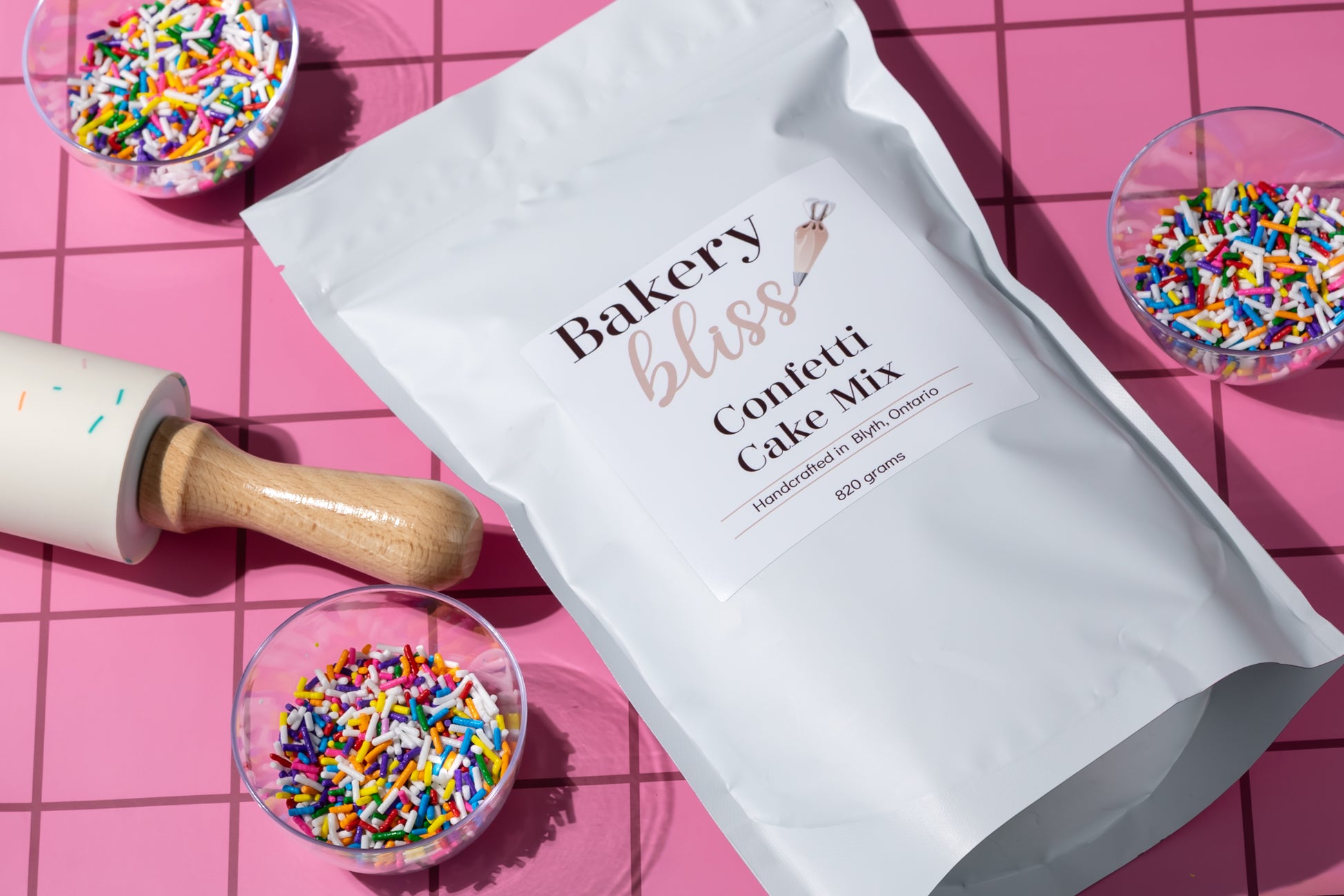 Bakery bliss confetti cake mix package with colorful sprinkles and a rolling pin on a pink grid background