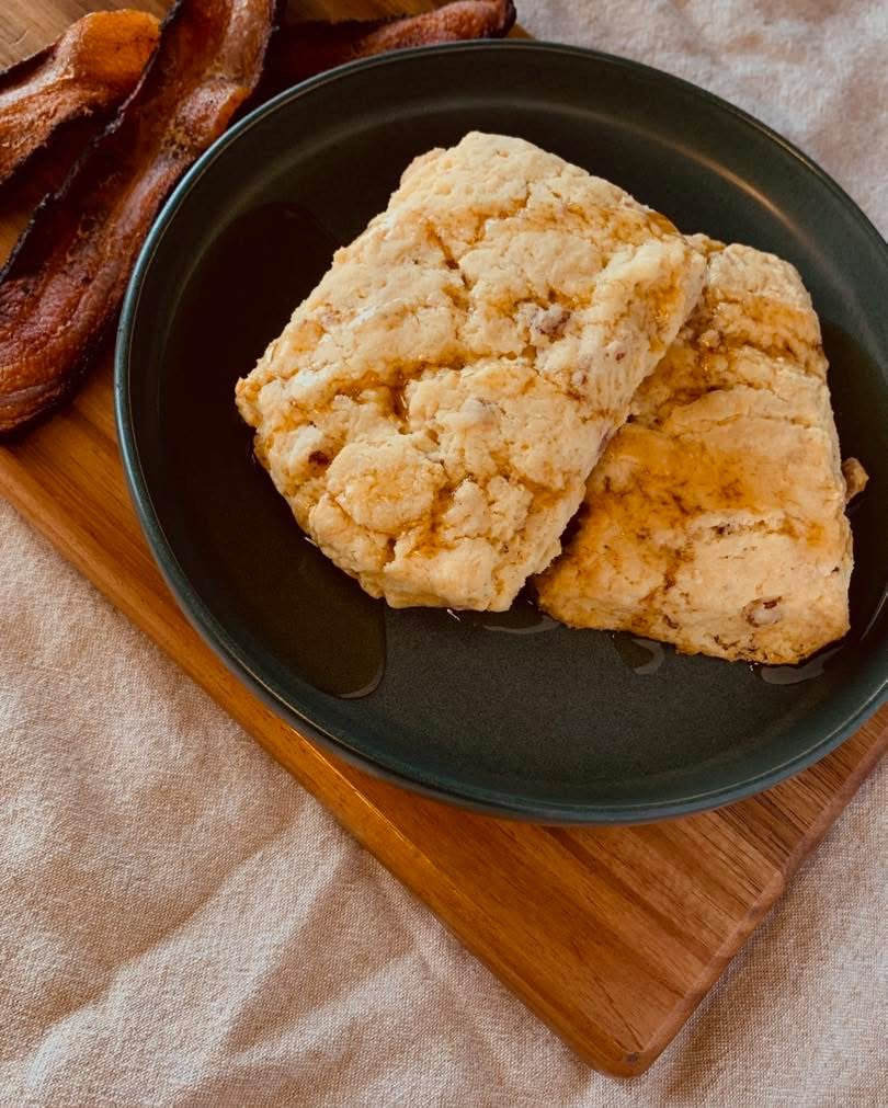 Two maple bacon scones on a dark green plate with bacon in the background
