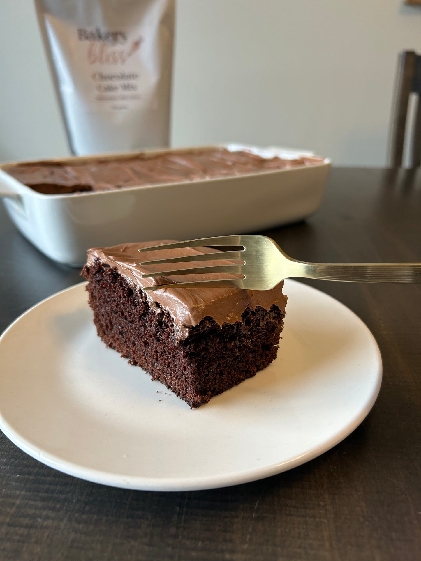 Slice of chocolate cake on a white plate with a gold fork, blurred background