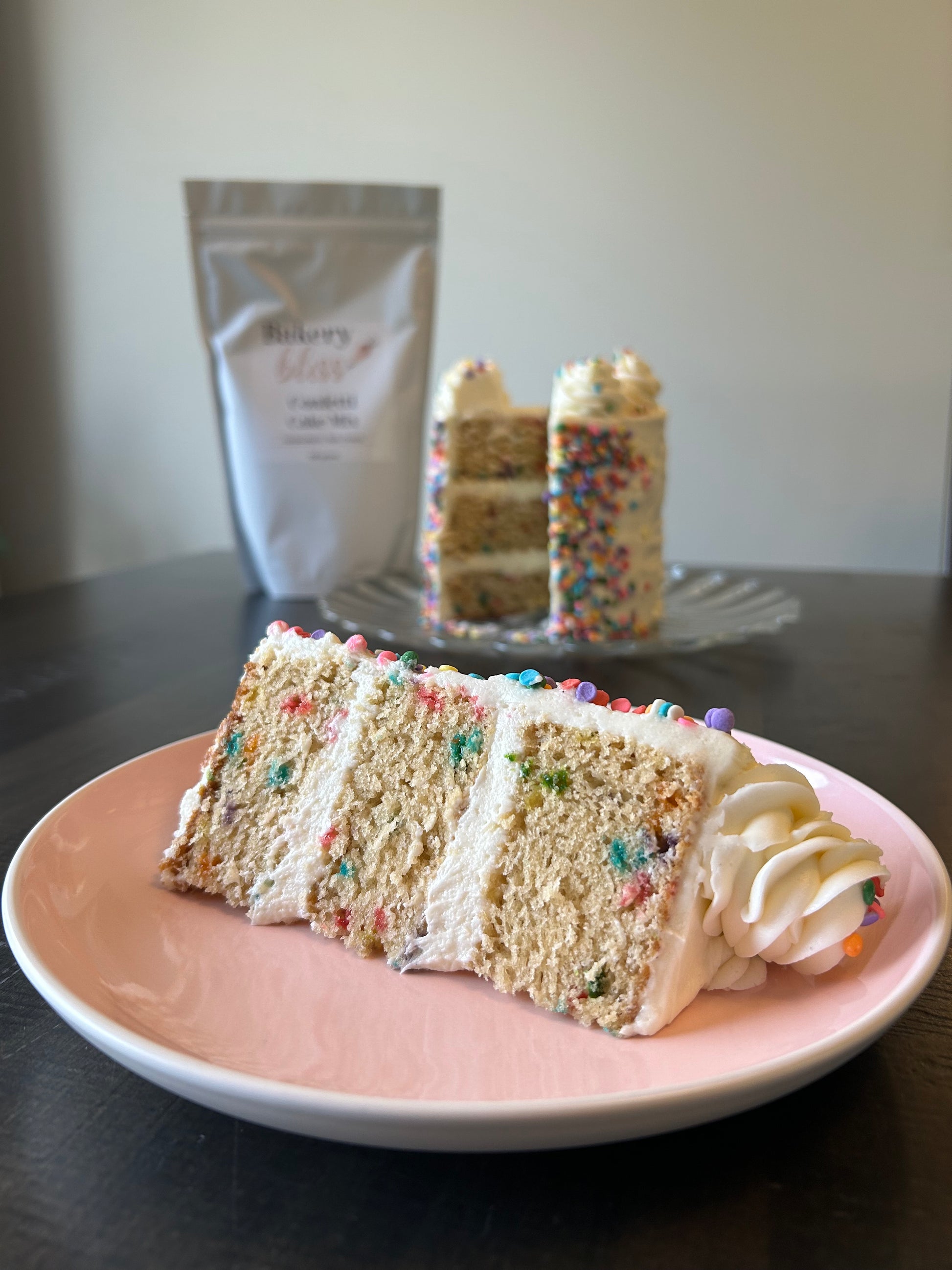 Slice of layered cake with colorful sprinkles on a pink plate
